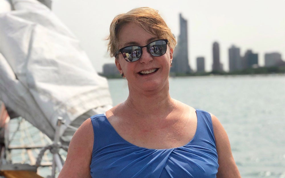 A woman stands on a boat with a city skyline behind her in the distance