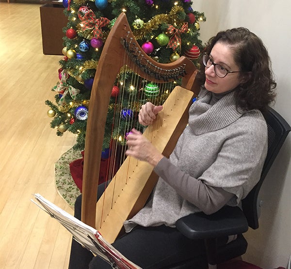 A woman plays the harp; Christmas decorations are visible in the background