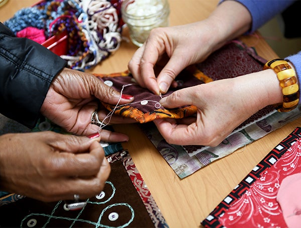 Two pairs of hands hold needles to quilt fabric with