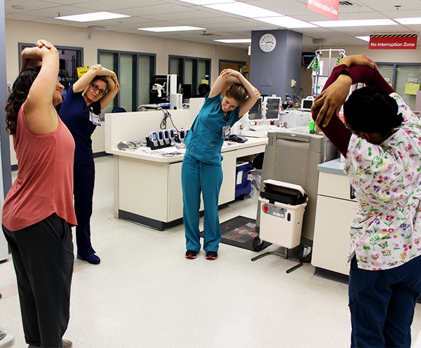 Individuals line a hallway stretching their arms overhead 