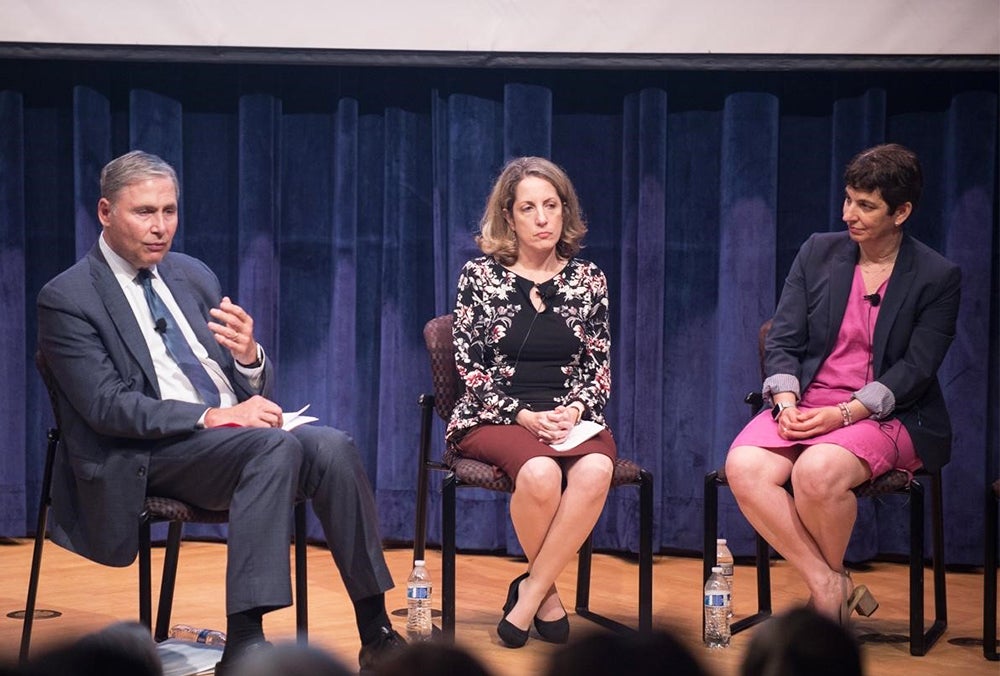 Three individuals sit on chairs onstage