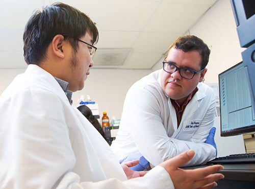 Two researchers in white lab coats talk with each other