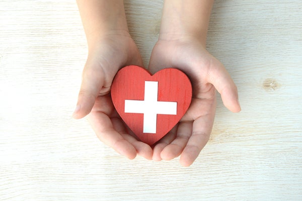 Closeup image of hands holding a a red heart inscribed with a medical cross 