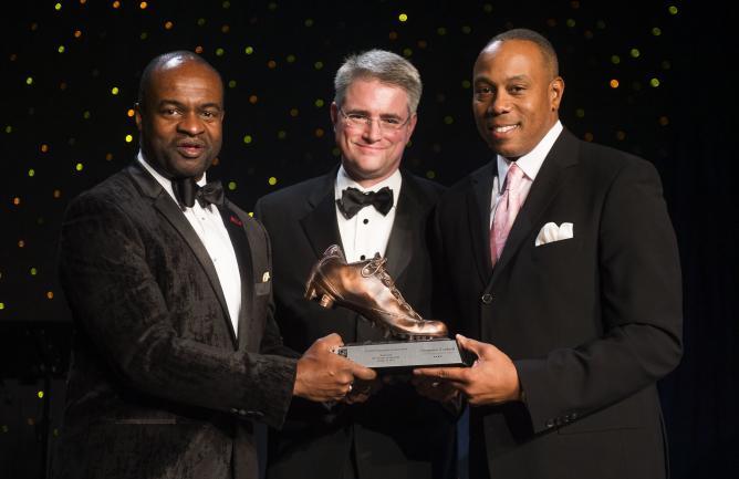 Three men hold a trophy of a shoe