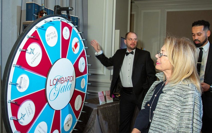 A woman regards a prize wheel as two men look on