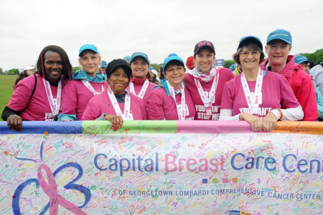 A group of women hold a banner for Capital Breast Care Center at a charity walk