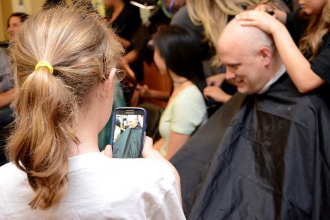 A girl takes video of a man getting his head shaved