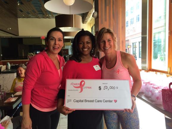Three women stand together holding an oversized check