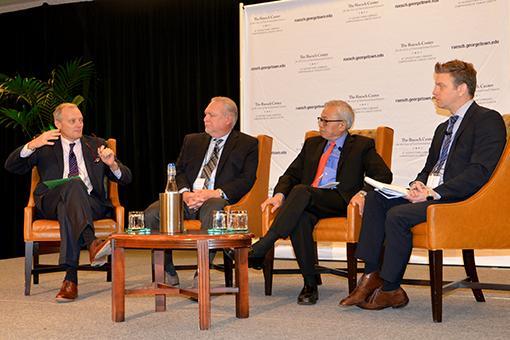 Four men sit in chairs onstage