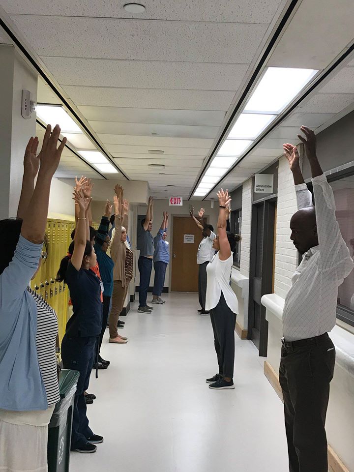 Photo taken of Alison Waldman leading staff members in a MedStar Georgetown University Hospital lab through a 5-minute stretch break. Staff line the hallway holding their arms up mid-stretch.