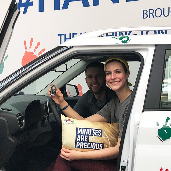 Two people smile from the front seats of a car