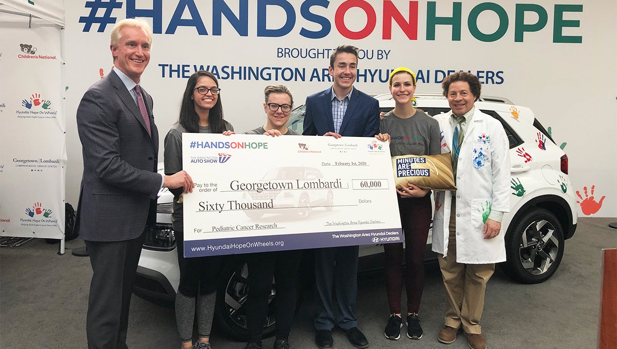 A group of people hold a large check in front of a Hyndai Venue at the Auto Show