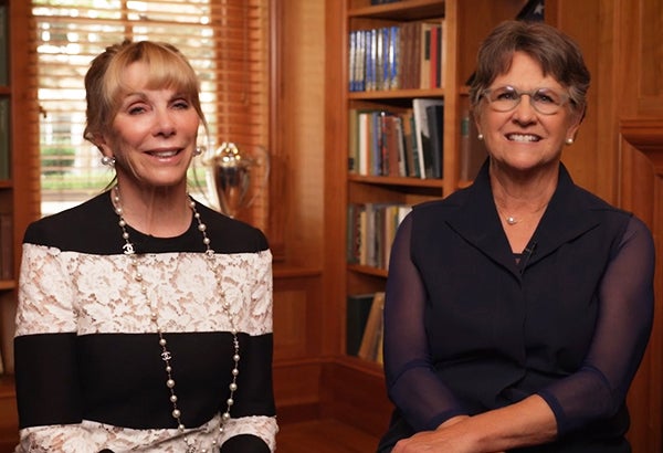 Two women sit in a wood-paneled room