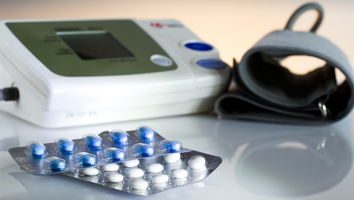 A blood pressure monitor with pills in the foreground