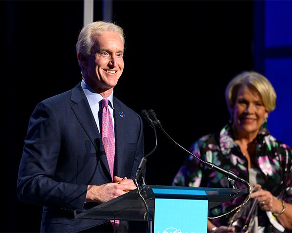 Kevin Reilly speaks at a podium while Laurie Lapeyre looks on