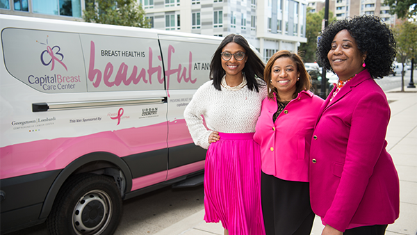 Three women stand with a van for Capital Breast Care Center outreach