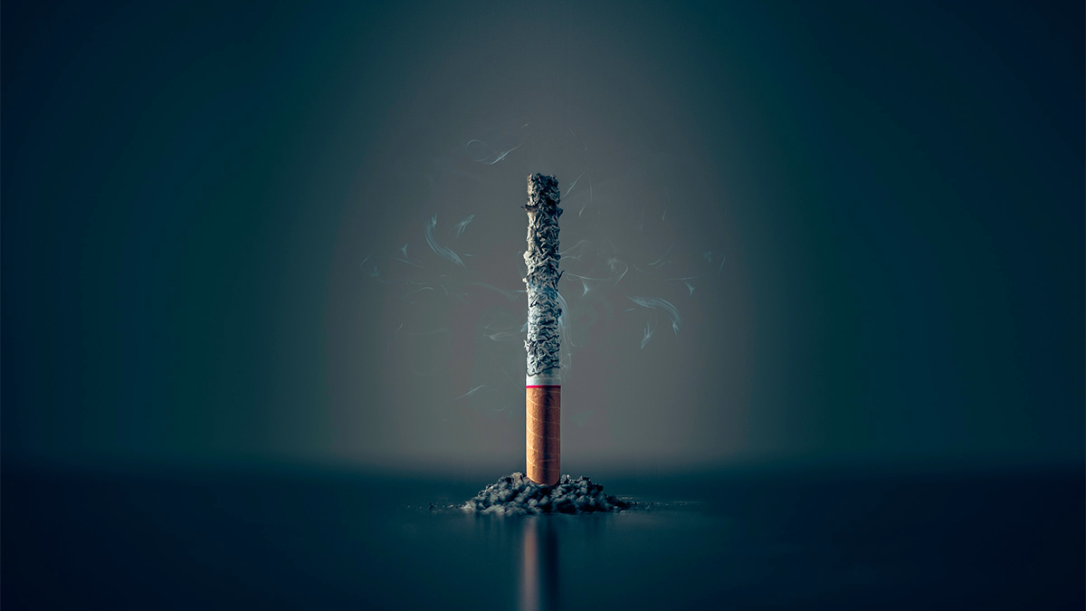 A cigarette stands on end, nearly burned to ashes