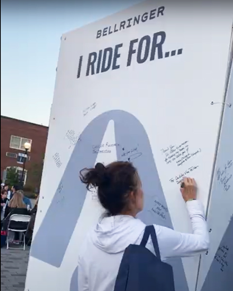 A woman writes on a large sign at BellRinger with the heading I ride for