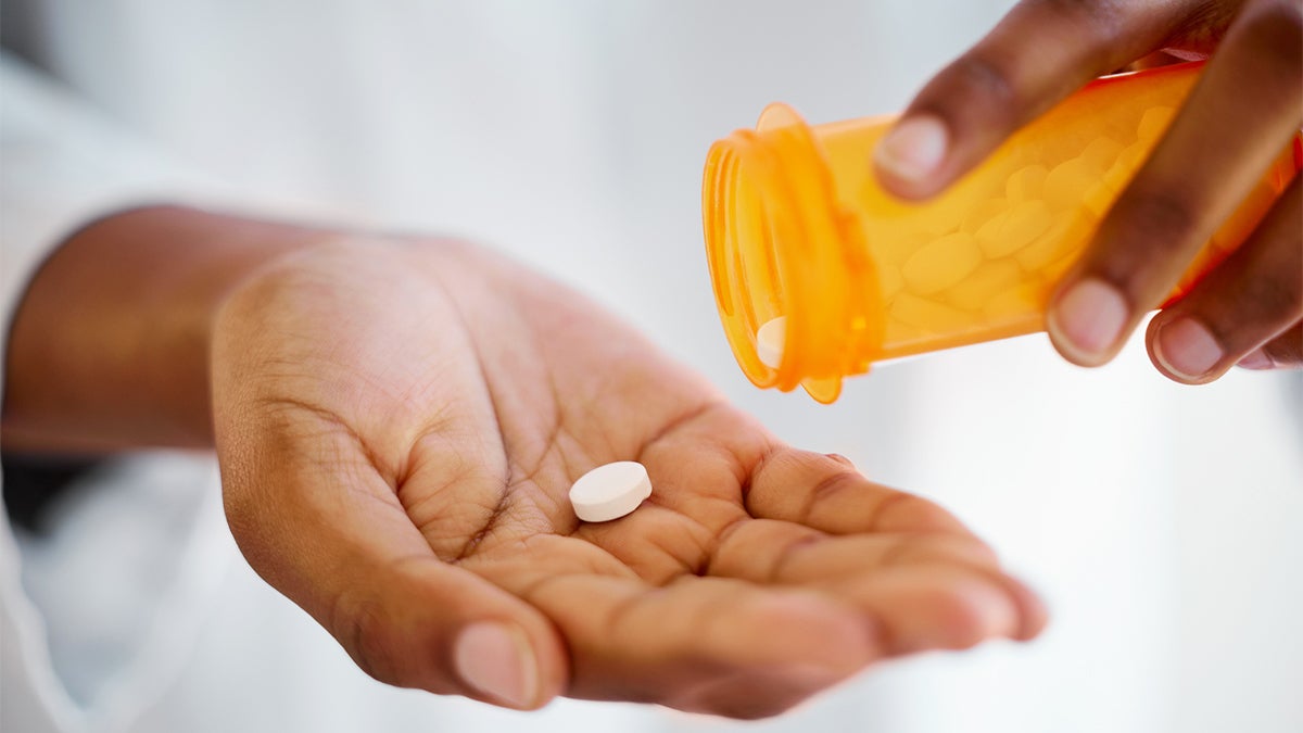 A person pours a single white pill into their open palm from a pill bottle