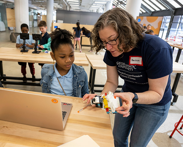 Becca works with a young student using a computer to program a robot