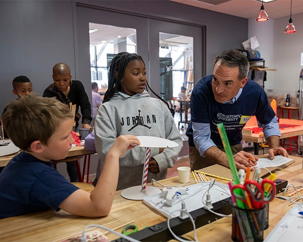 Ken speaks with two students who are building a device out of paper plates and straws