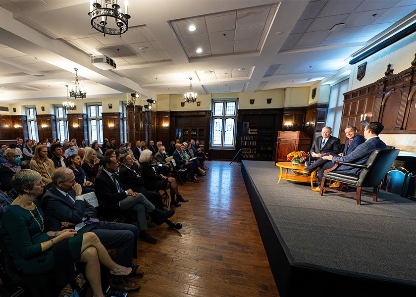 The three featured speakers sit in chairs onstage before an audience