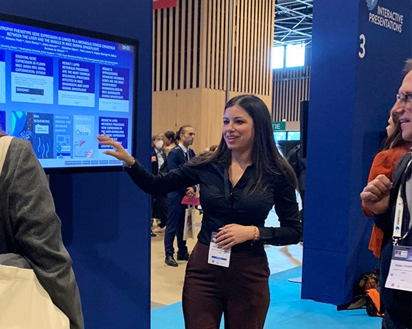 Geraldine Vitry motions toward a screen displaying her research abstract while two individuals look on