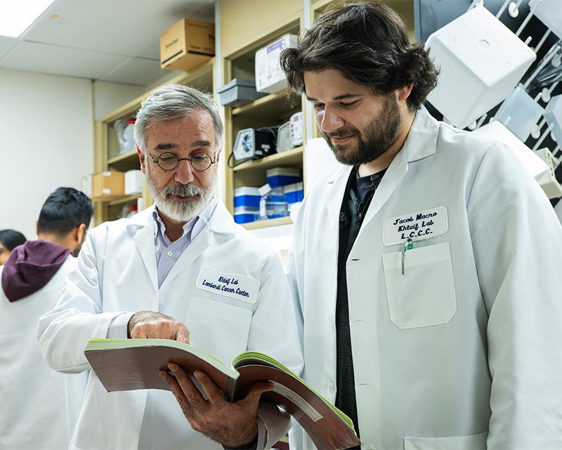 Dr. Khleif points to a journal article as a student looks on in his lab