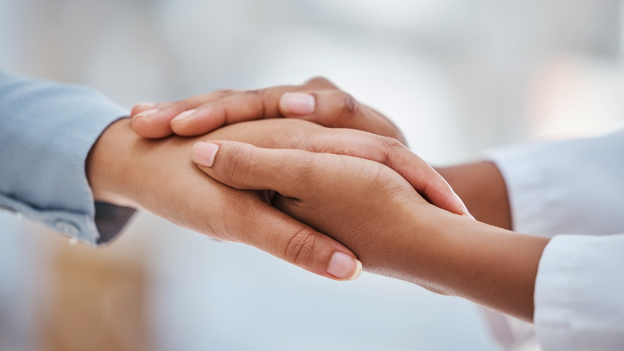 A person's hands hold a another person's hand in a gesture of comfort