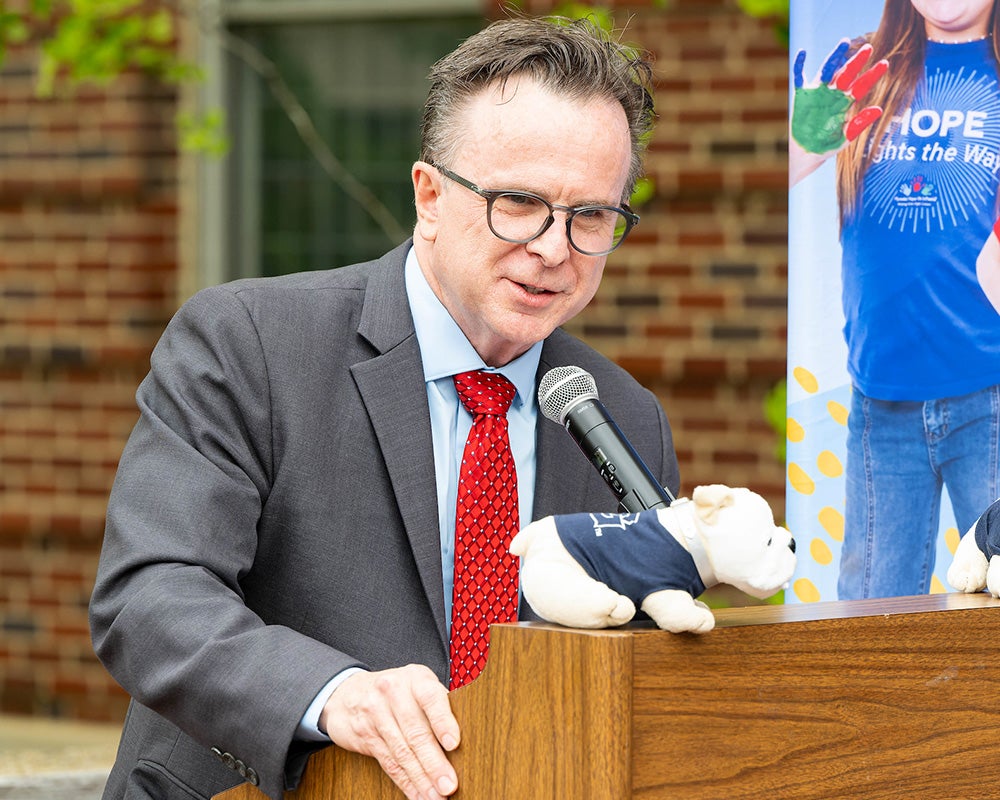 Dr. Beauchamp speaks from a podium at the event, two stuffed bulldogs perch on the podium before him