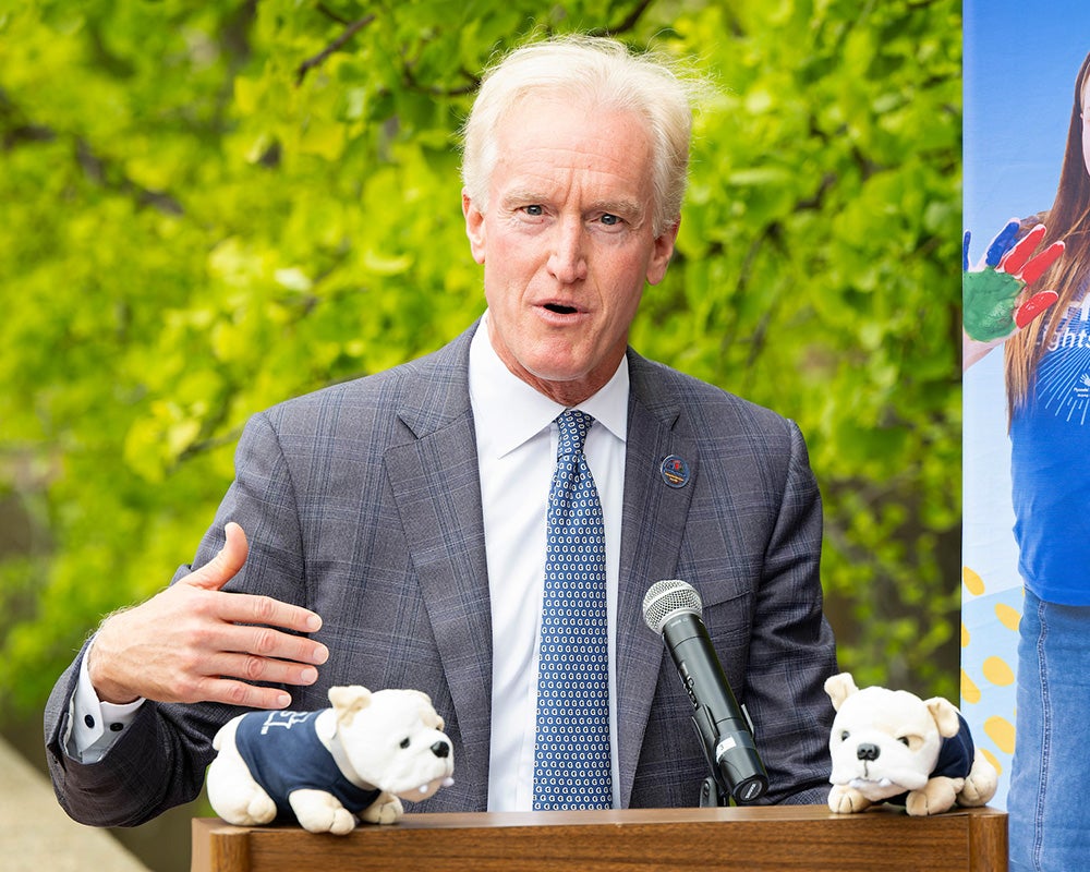 Kevin Reilly speaks from a podium at the event, two stuffed bulldogs decorate the podium