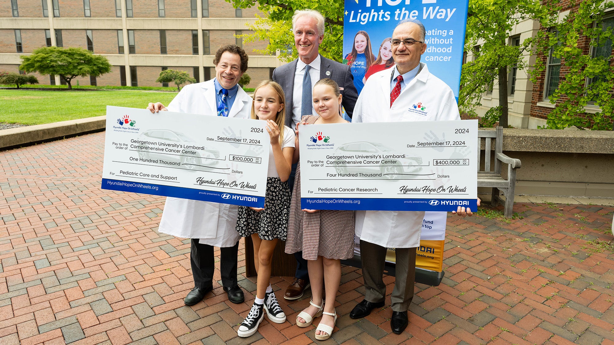 A group stands with individuals holding two large checks