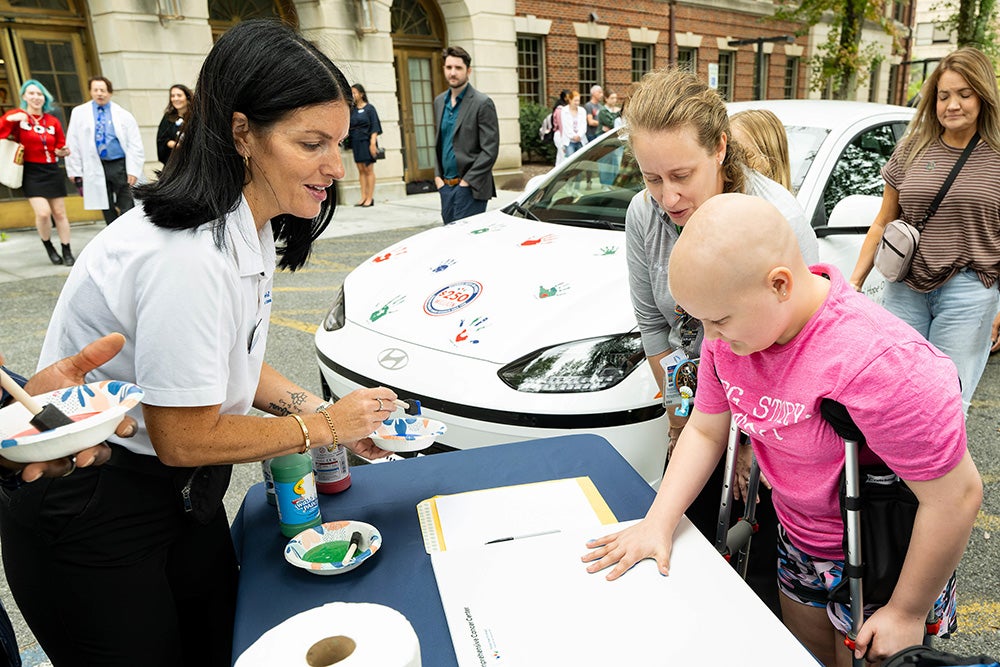 A young cancer patients places a painted hand on a piece of paper while adults look on