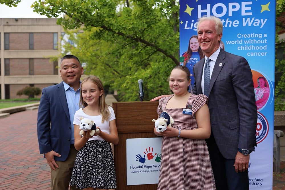 Two girls holding stuffed bulldogs stand in front of Hyundai's Tran and Reilly