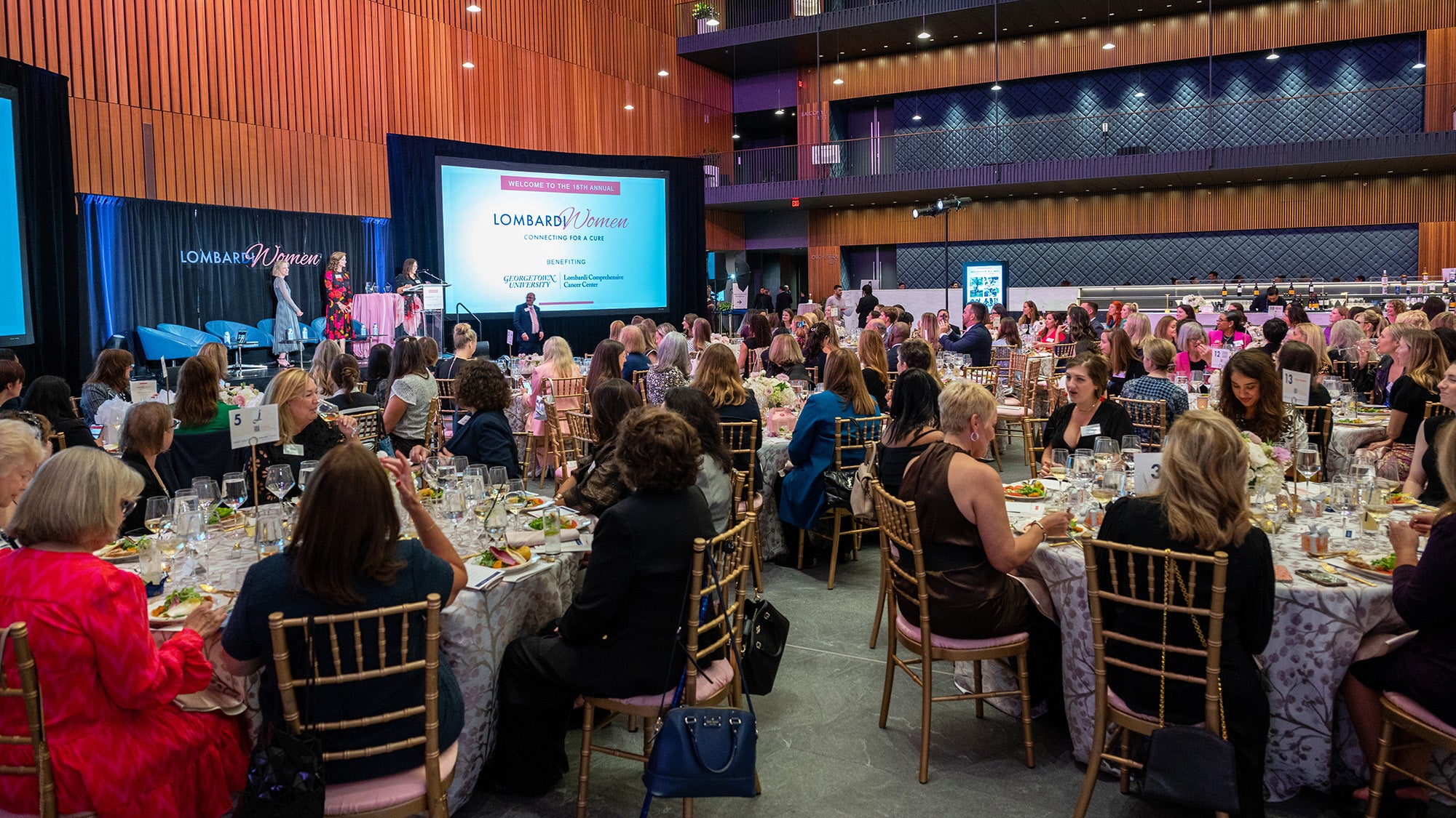 A view of the event showing tables of attendees before a stage with a large screen and podium