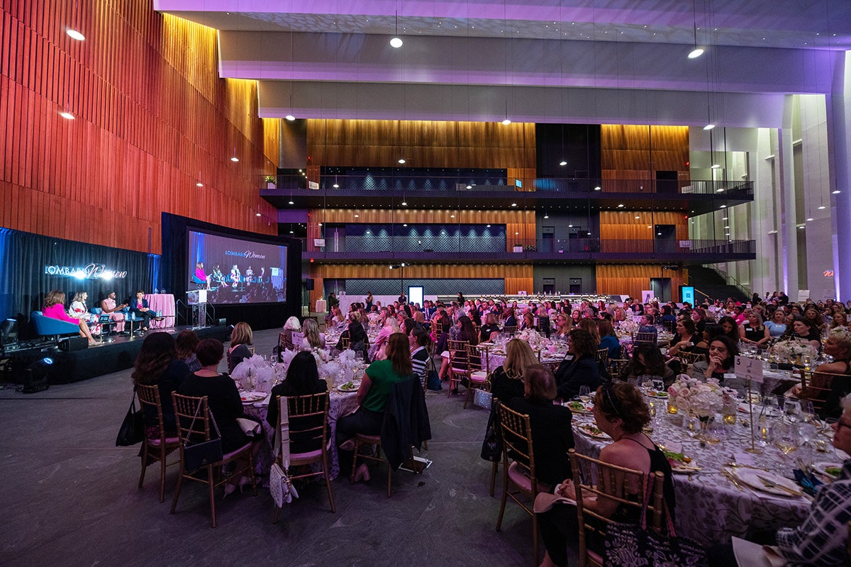 an overview of the room at Lombardi Women that shows the panelists onstage plus tables of attendees