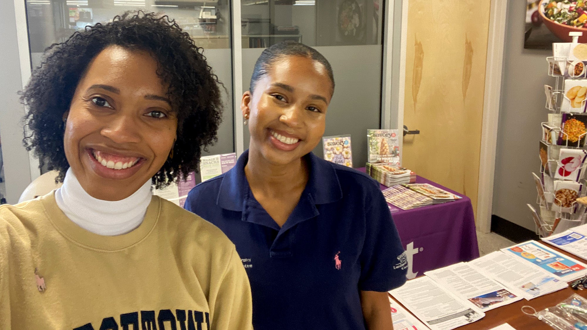 Two Black women stand with a table in the background