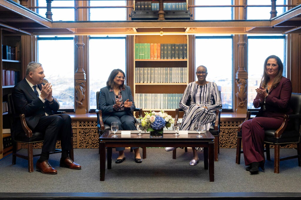 Four individuals sit in chairs on a stage area in Riggs Library before an audience