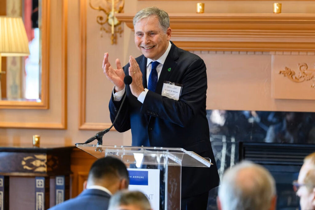 Dr. Weiner claps his hands while standing behind a podium