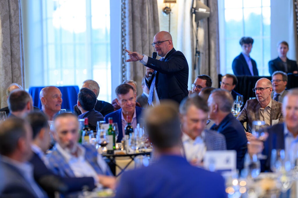 The Men's Event auctioneer gestures to a bidder amid tables of attendees