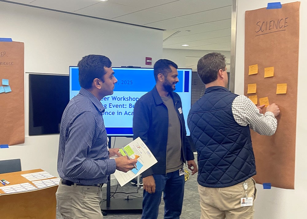 Three attendees add sticky notes to a poster