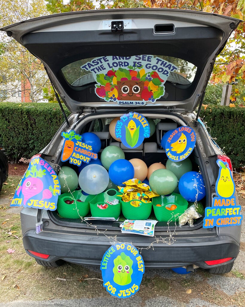 A car's open trunk is filled with balloons, signs and buckets of fruit and healthy snacks