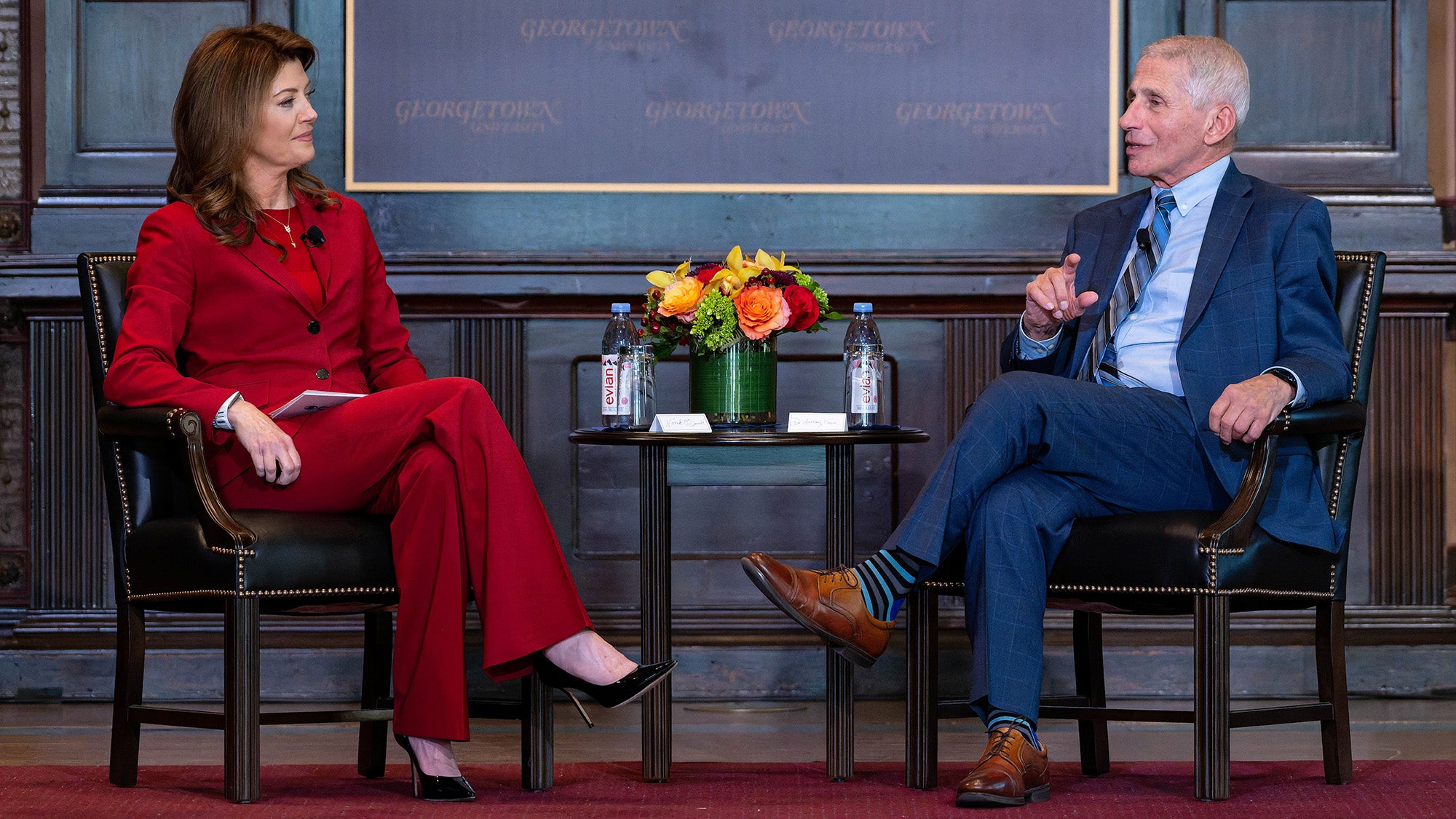 Norah O'Donnell and Anthony Fauci sit opposite each other onstage in Gaston Hall