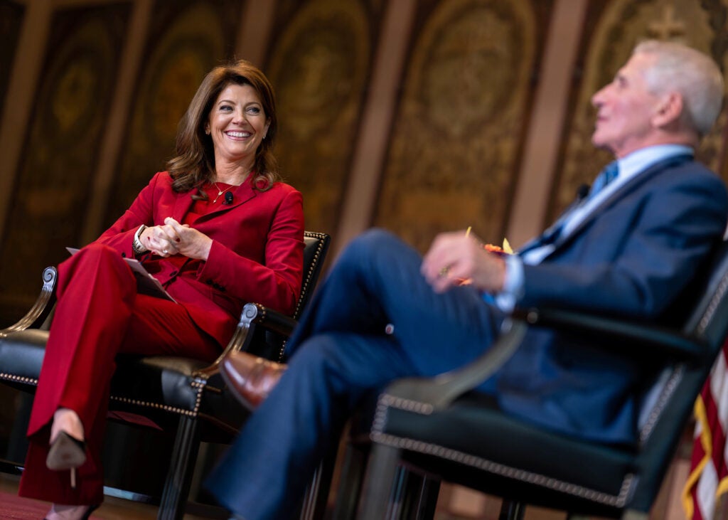 Norah O'Donnell smiles as Anthony Fauci speaks while both are seated onstage in Gaston Hall