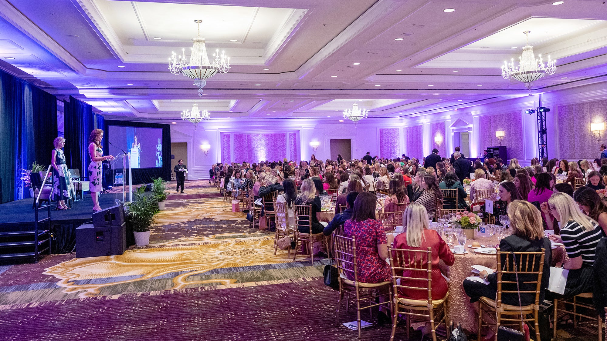 A ballroom filled with participants in the Lombardi Women gala and two of the event organizers on a dais at the front of the room