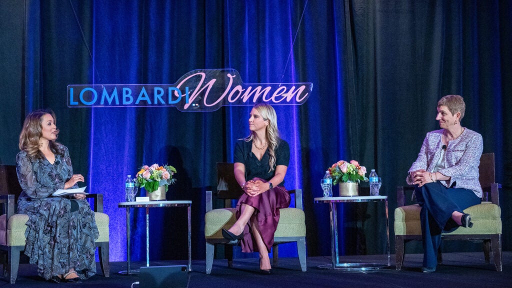 The three panel participants sit in chairs on the dais as they speak to one another at the Lombardi Women gala