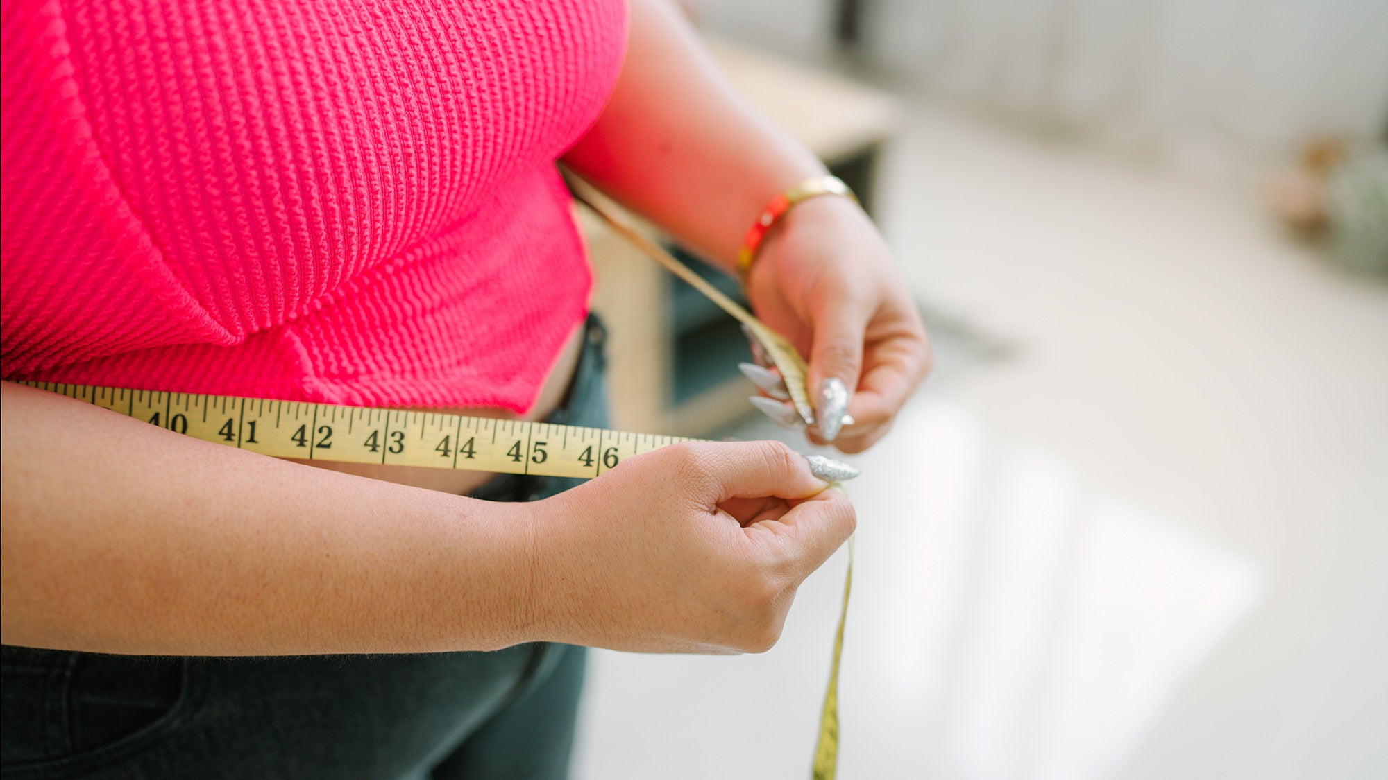 A woman measures her waist circumference with a tape measure