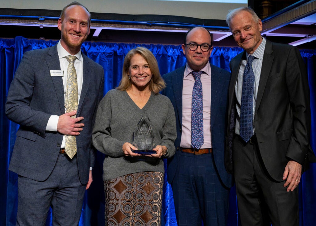Four individuals stand together, one of them is Katie Couric holding an award