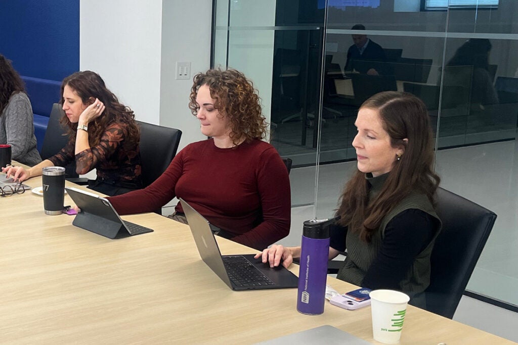Three trainees work at their laptops while seated at a conference table