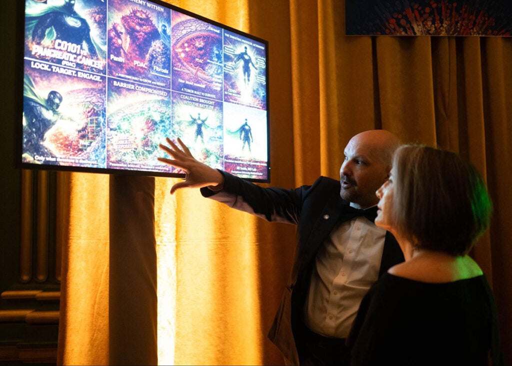 A man gestures toward a display panel featuring illustrations explaining the research of Dr. Jill Smith